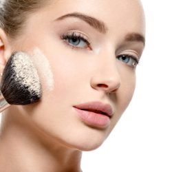 Young girl applies  powder  on the face using makeup brush.